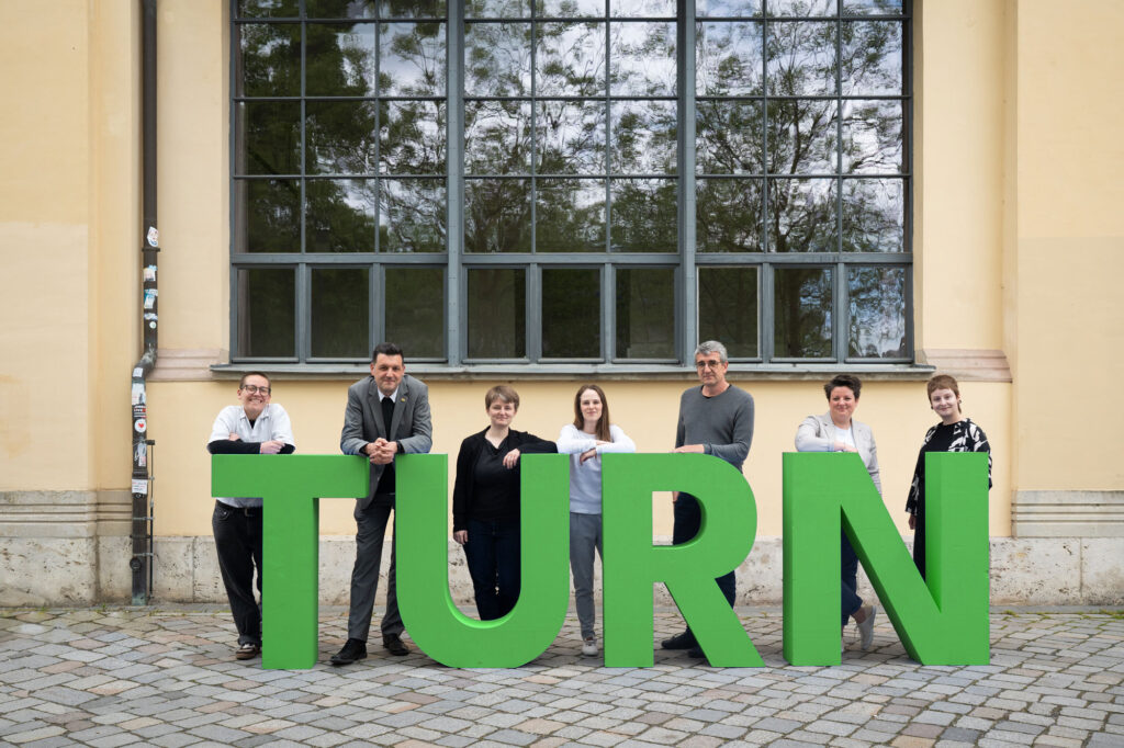 TURN26-Team mit TURN Buchstaben vor dem Hauptgebäude (v.l.n.r. Jules Dahrendorf, Prof. Peter Benz, Anna-Lena Öhmann, Elisa Kirbst, Dr. Andreas Mai, Stephanie Wolf, Larissa Barth)
